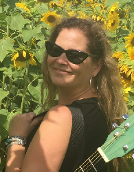 Michele Shell Anders a musician in a field of sunflowers with a guitar